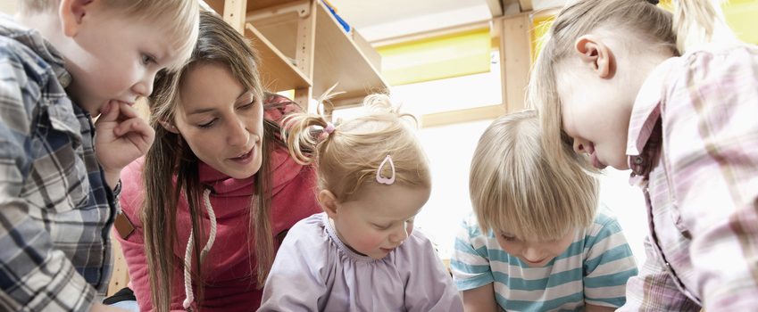 Tagesmutter sitzt mit Kindern auf dem Boden und spielt