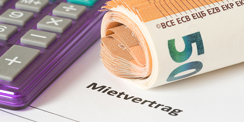 Auf einem Mietvertrag liegen ein Taschenrechner und 50 Euro Banknotenbündel