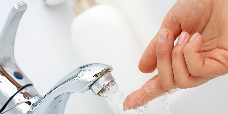 Eine Person hält sein Finger unter den laufenden Wasserhahn.